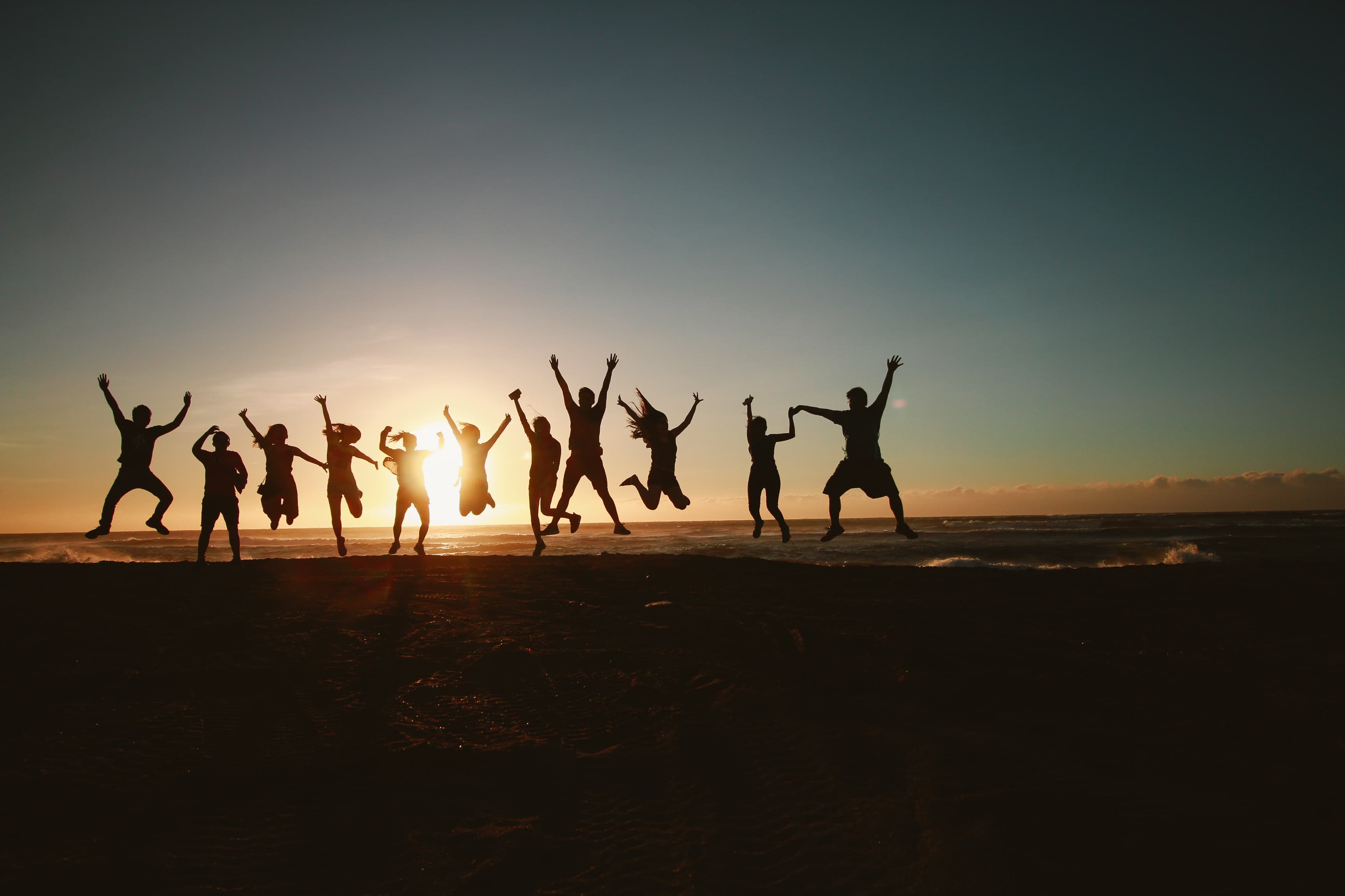 Community of people jumping together at sunset