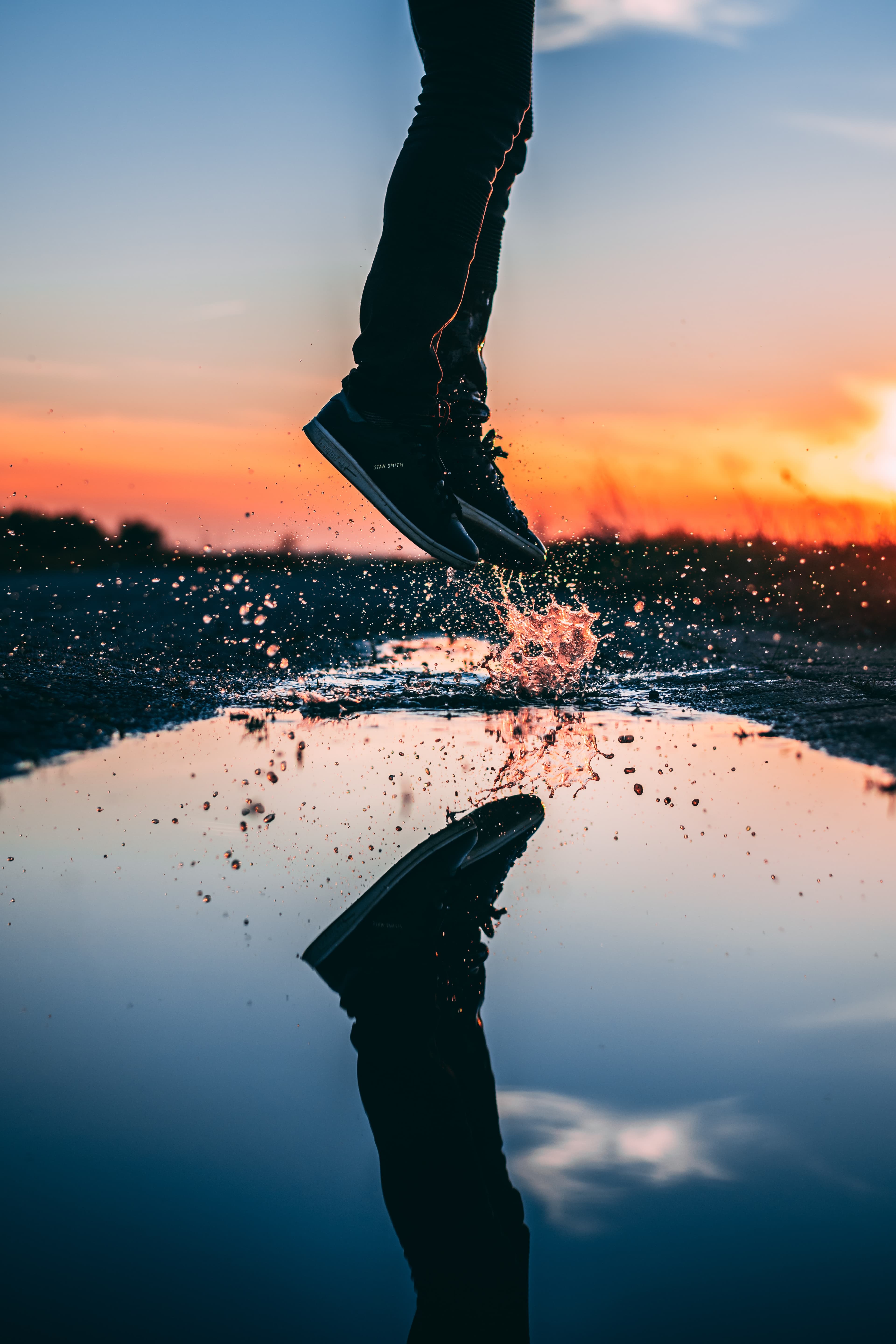 Person jumping through a puddle at sunset